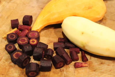 Purple carrots and potatoes being prepared for roasting.