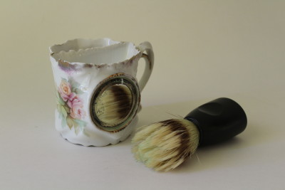 A vintage shaving mug and a modern shaving brush.